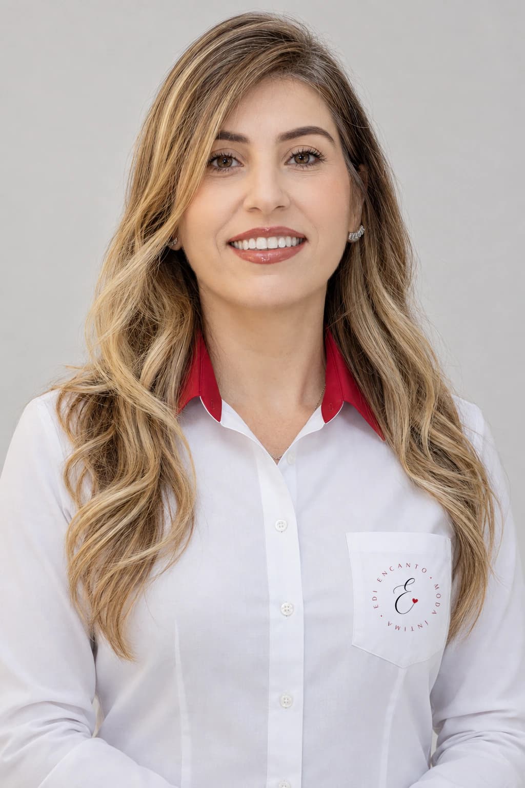 Retrato da Edilaine, a Edi da Edi Encanto, de camisa branca com gola vermelha e o emblema da loja no bolso